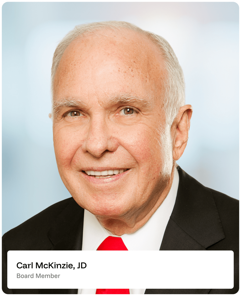Smiling older man with short white hair wearing a black suit, white shirt, and red tie, posed in front of a softly blurred background. Text below reads: Carl McKinzie, JD, Board Member..