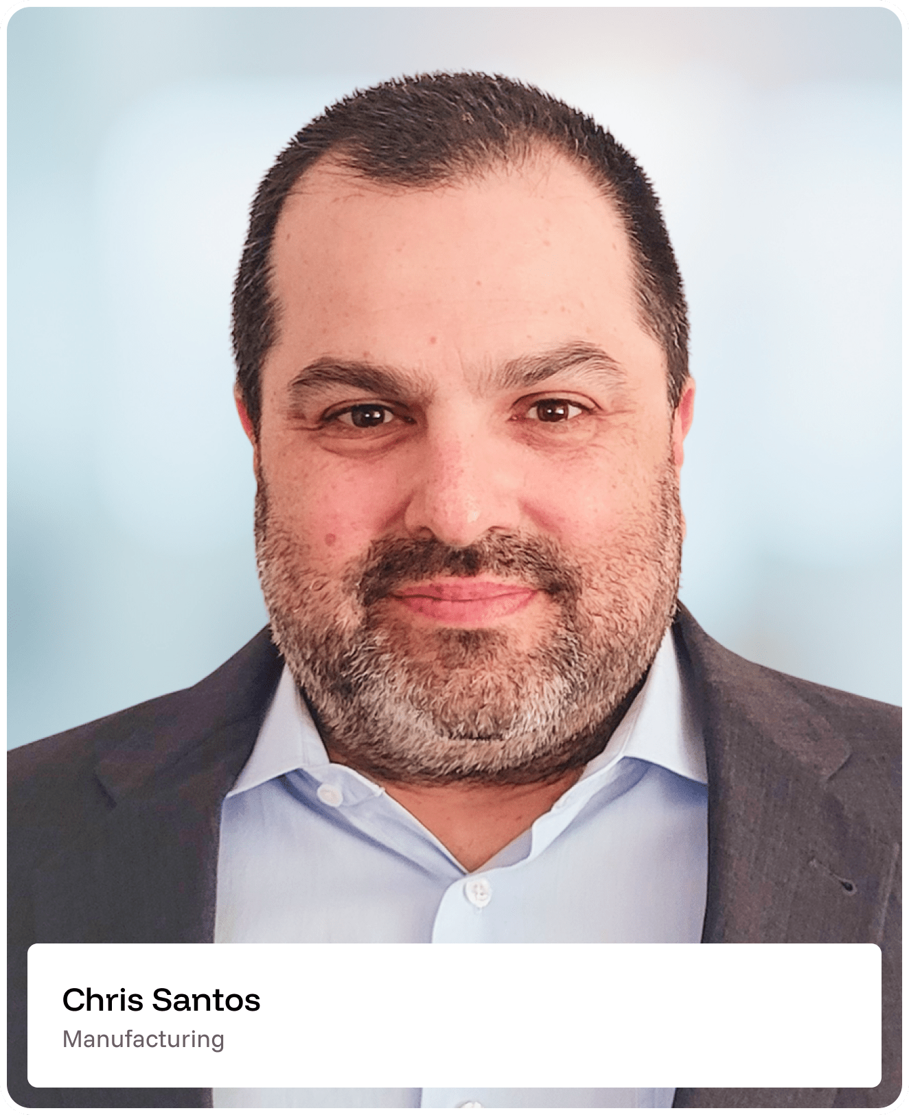 A man with short dark hair and a beard, wearing a suit jacket and light blue shirt, is shown smiling slightly. The background is blurred. Text at the bottom reads: Chris Santos, Manufacturing..